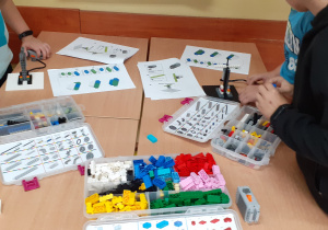 Chłopcy budują modele rakiet według instrukcji. Na stoliku widać otwarte pudełka z klockami LEGO.